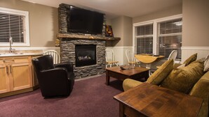 A living room with a stone fireplace, a flat-screen TV mounted above it, a wooden dining table, and a sofa.