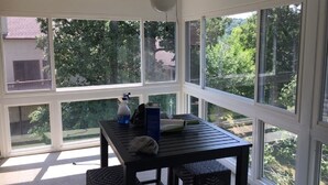 Una veranda con tavolo, sedie, ventilatore a soffitto e ampie finestre che offrono vista sul panorama esterno.