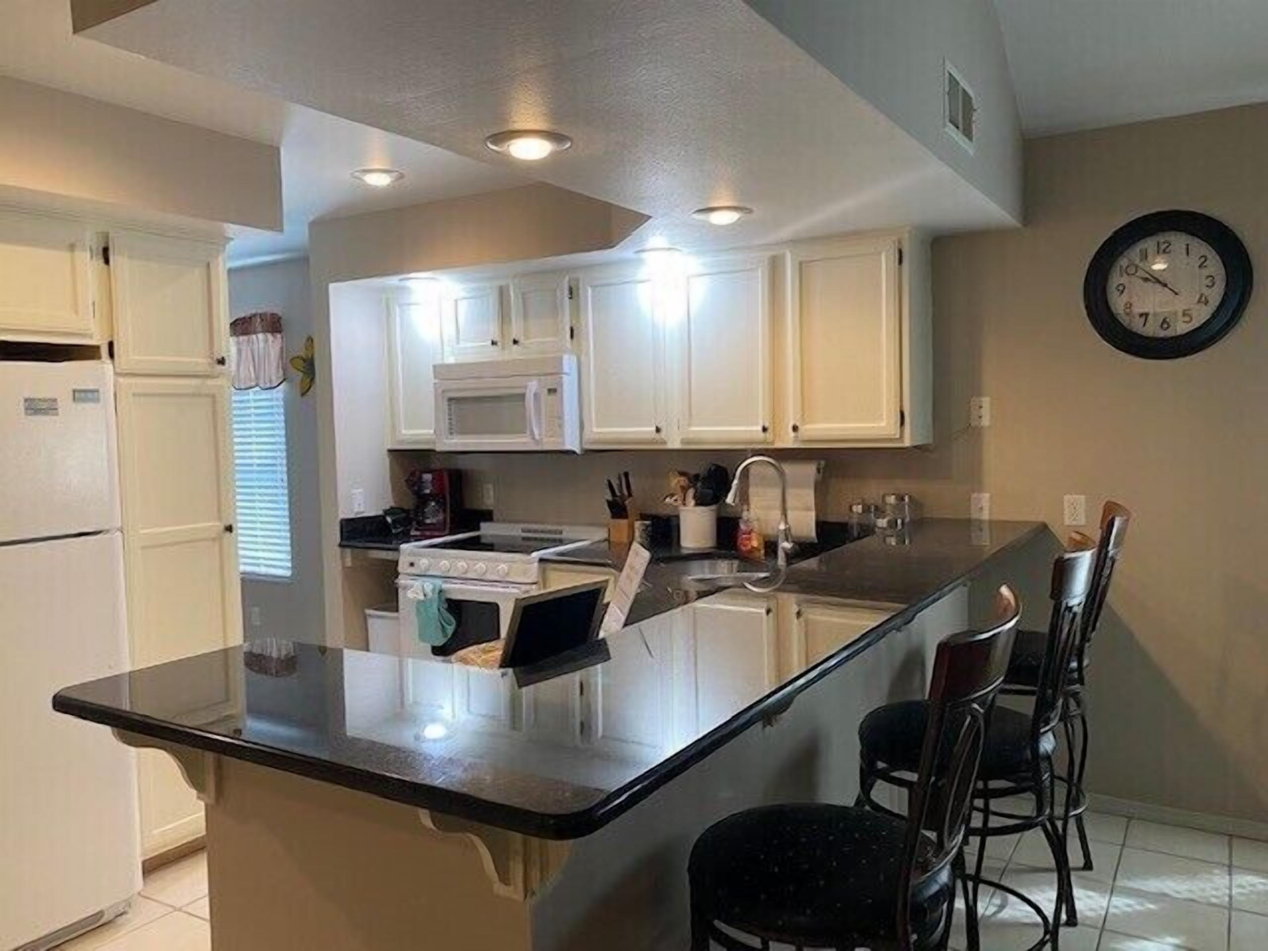 A kitchen with white cabinets, a microwave, a stove, a sink, and a clock on the wall.