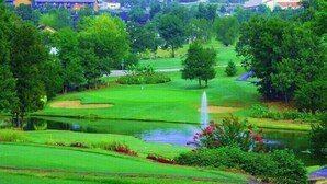 Un campo da golf con uno stagno, alberi e un edificio con la scritta 'WELK' sullo sfondo.