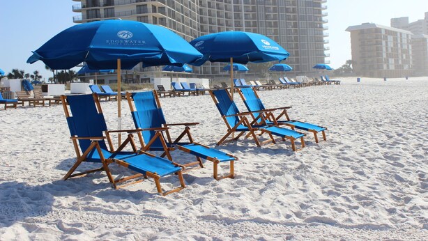 Une plage avec des parasols bleus et des chaises longues en bois.