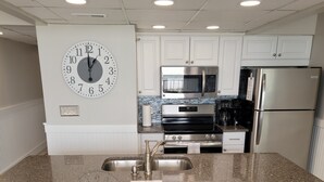 Une cuisine moderne dotée d’un plan de travail en granit, d’appareils électroménagers en acier inoxydable et d’une horloge murale.