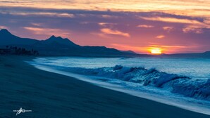 A beach with waves, mountains, and a sunset. - Las Mananitas-Awesome Luxury Beachside Condo in Cabo! (san jose del cabo)