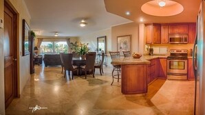 A spacious kitchen with a central island, a dining area with a table and chairs, and a view of the outdoors through large windows. - Las Mananitas-Awesome Luxury Beachside Condo in Cabo! (san jose del cabo)