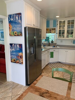 A modern kitchen with white cabinets, a stainless steel refrigerator, and a sink. There are two wall art pieces with motivational quotes. - Cozy Slice Of Paradise Just Steps From The Beach!! (Newport Beach)
