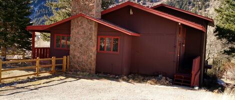 A rustic cabin with a stone chimney, red exterior, and a wooden porch.