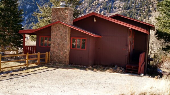 Une cabane rustique avec une cheminée en pierre, une façade rouge et une véranda en bois.