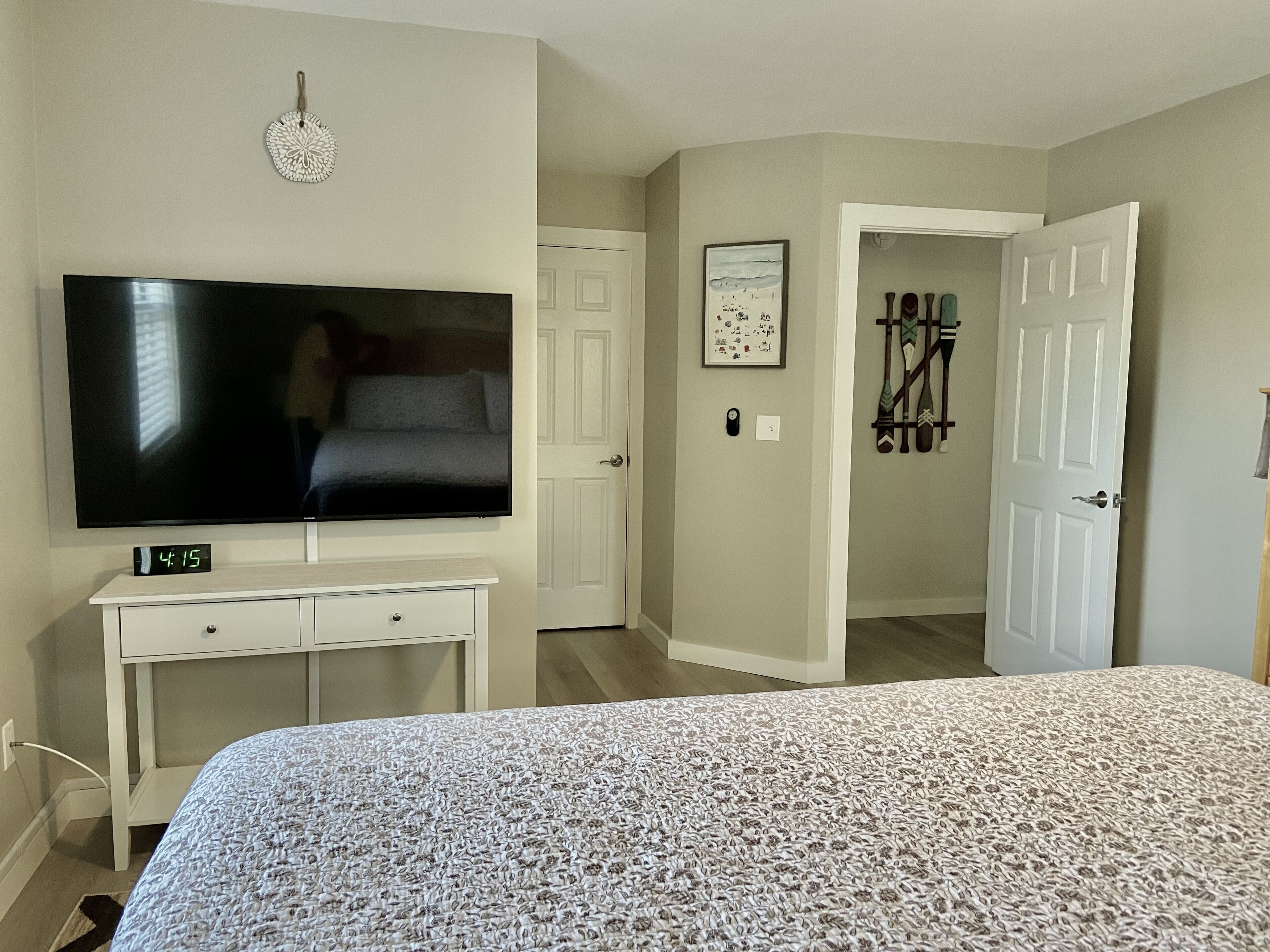 A bedroom with a bed, a TV, a dresser, a door, and a hallway.