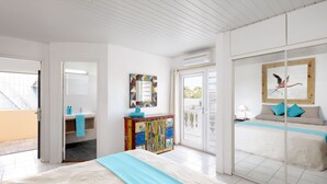 Ein Schlafzimmer mit Bett, einem farbenfrohen Schrank, einem Badezimmer mit Waschbecken und Handtuch sowie einem Balkon mit Aussicht.