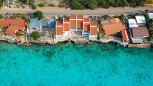 Eine Luftaufnahme einer Küstenlage mit mehreren Gebäuden, klarem türkisblauem Wasser und einer felsigen Küstenlinie.
