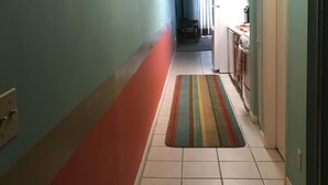 A narrow hallway with teal and red walls, a tiled floor, and a striped rug. - Check out new rates for summer (Panama City Beach)