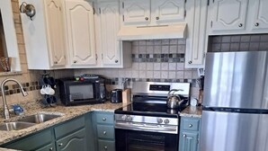 Una cocina con gabinetes blancos, un refrigerador de acero inoxidable, un horno negro y un microondas.