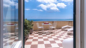 A balcony with a checkered floor, white chairs, a small table, and a potted plant.
