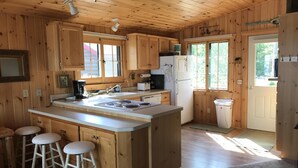 A wooden cabin kitchen with a central island, bar stools, a refrigerator, and a sink. - *HIGH DEMAND* Sugar Sand Beach & Cozy Cabin That Sleeps 10 on Pelican Lake!  (Merrifield)