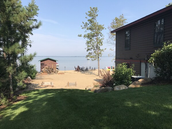 A cabin with a sandy beach area, a small shed, and a view of the lake.