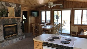 A cabin interior with a stone fireplace, wooden dining area, and a kitchen with a stove. - *HIGH DEMAND* Sugar Sand Beach & Cozy Cabin That Sleeps 10 on Pelican Lake!  (Merrifield)