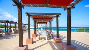 Een terras met tafels en stoelen onder een rood zonnescherm, met uitzicht op het water.