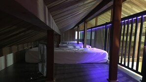 Un dormitorio con una cama grande, vigas de madera y vistas a través de una ventana con persianas verticales.