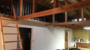 Habitación estilo loft con vigas de madera a la vista, una escalera, un sofá y una zona de cocina con mesa de comedor.