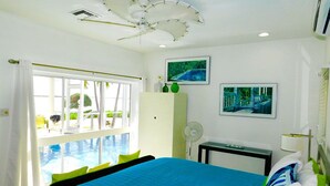 A hotel room with a large bed, a ceiling fan, a window with a view of a pool, and artwork on the walls. - The Pools #1- the Luxury Beachfront Hideaway with Private Pool (North Side, Cayman Kai,)