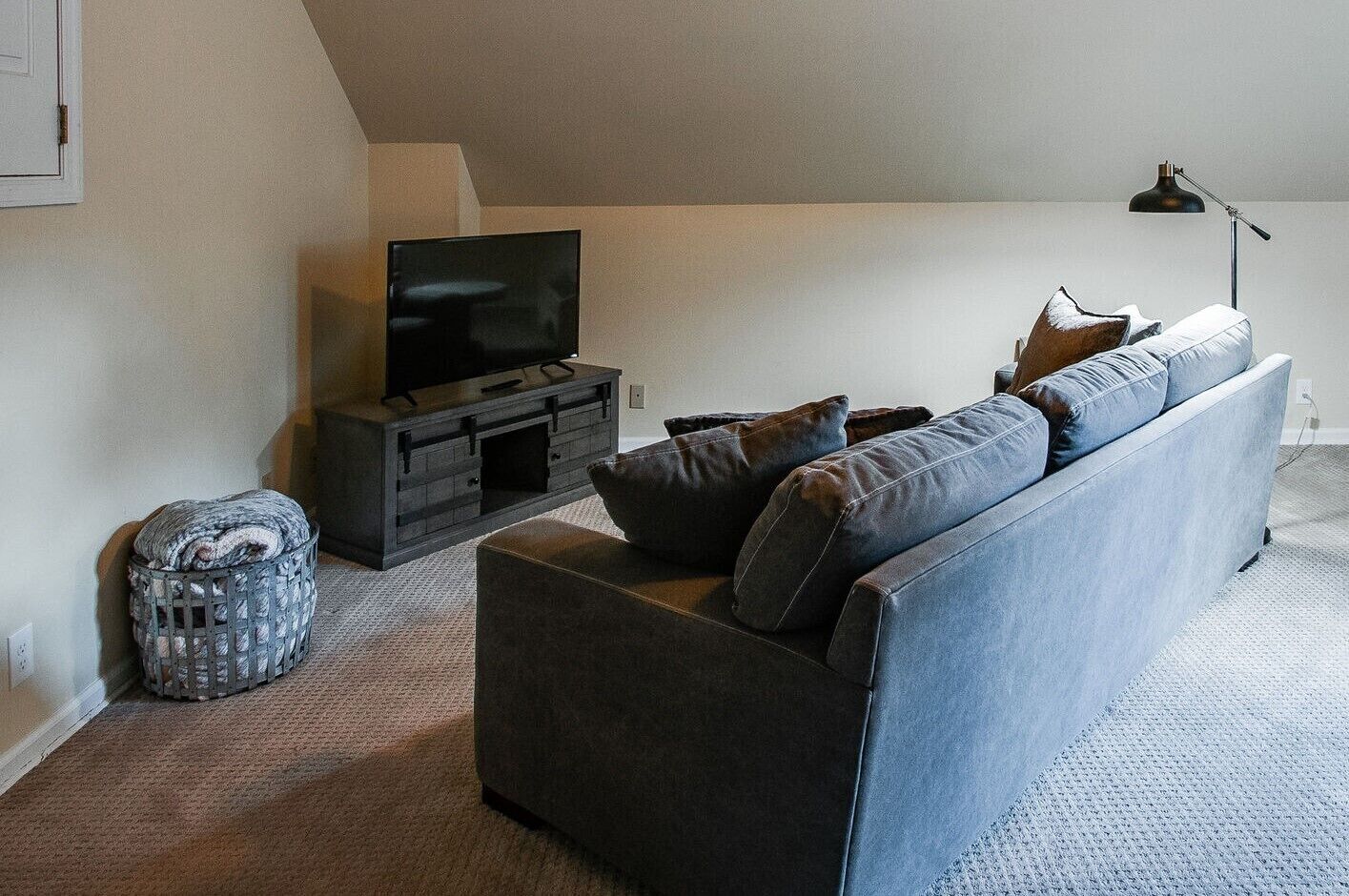A modern living room with a dark grey sofa, a flat-screen TV on a wooden stand, a small side table, and a lamp.