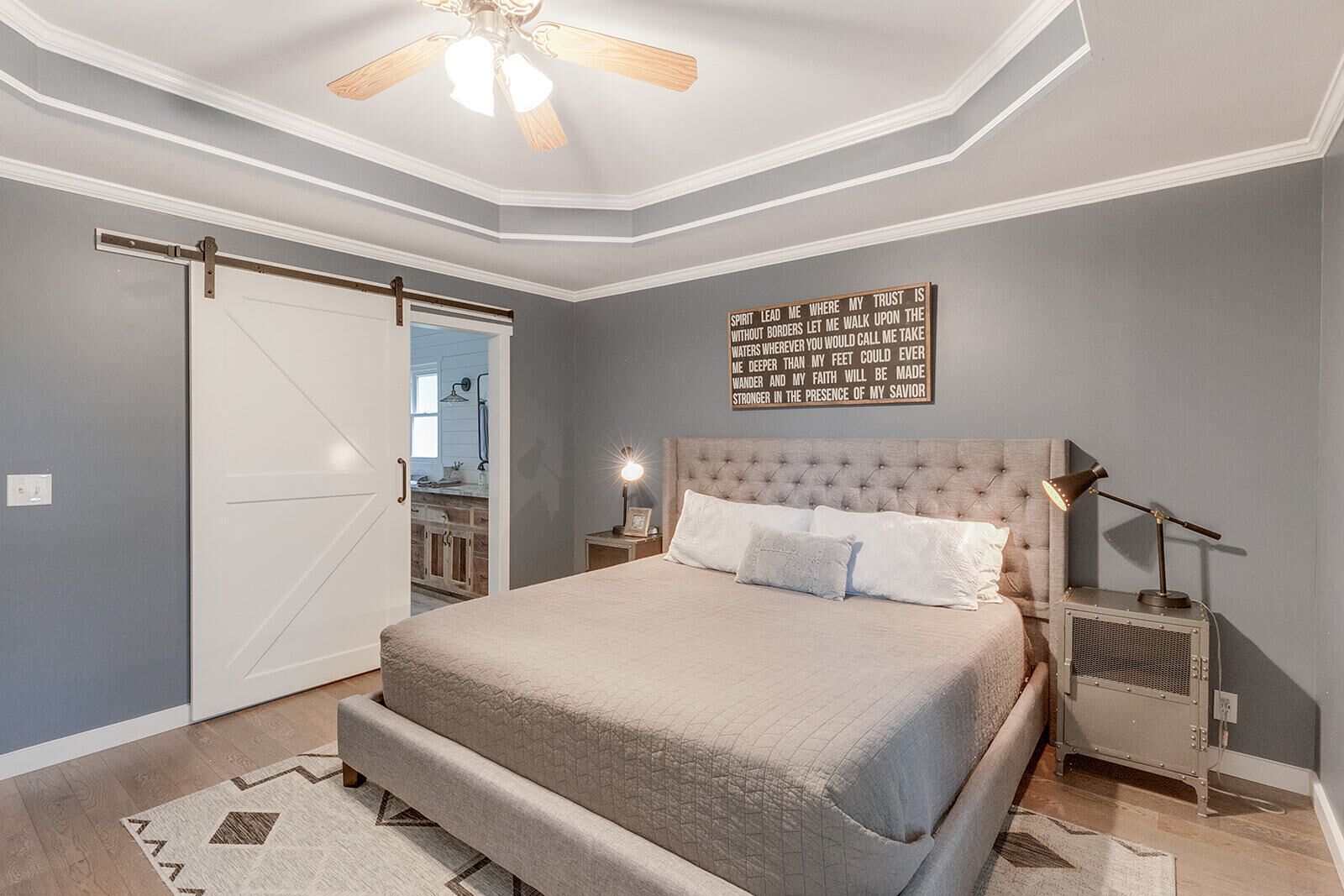 Une chambre dotée d’un grand lit, d’un ventilateur de plafond, d’une lampe fixée au mur et d’une porte donnant accès à une salle de bain.