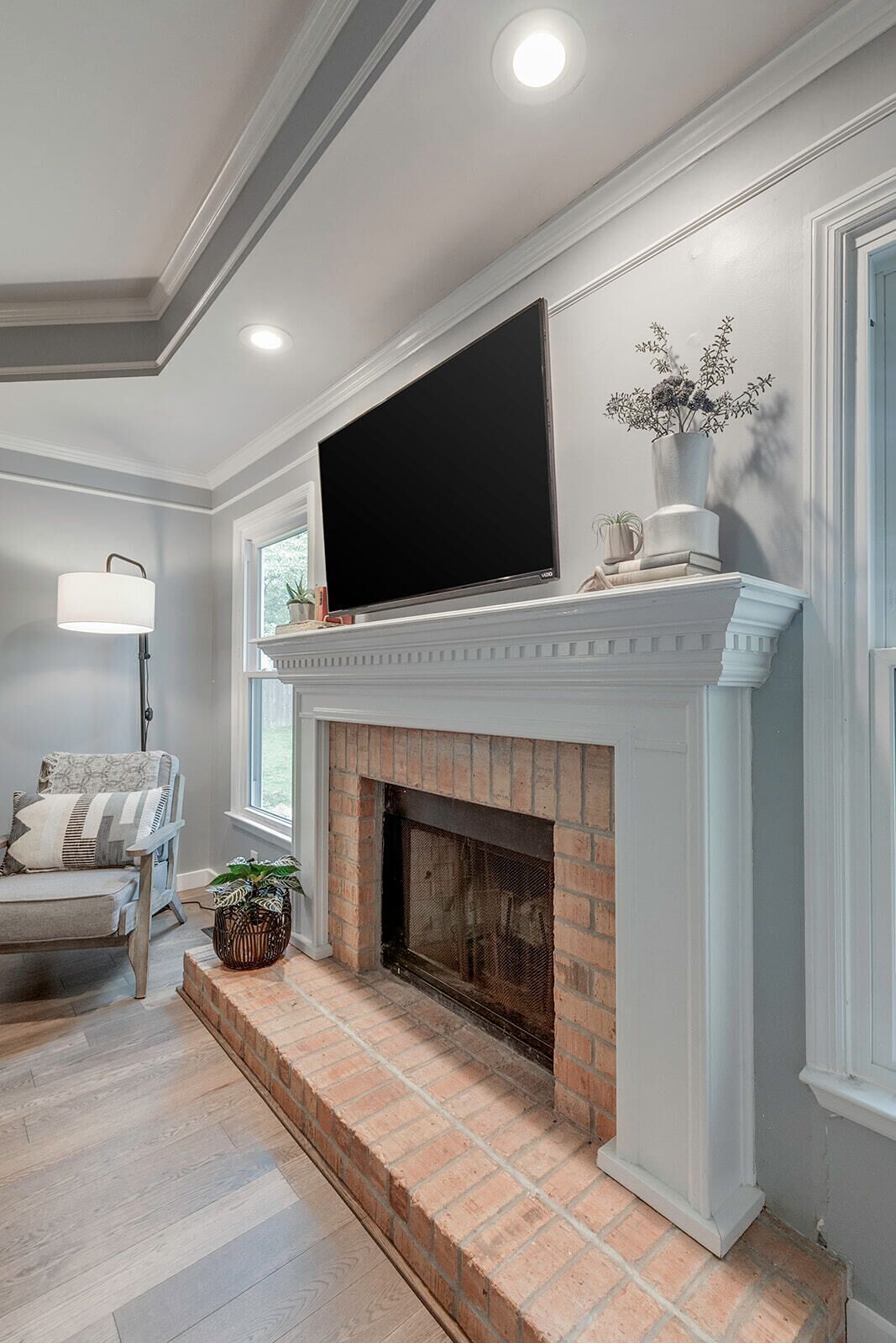 A living room with a fireplace, a flat-screen TV mounted above it, a comfortable chair, and a potted plant.