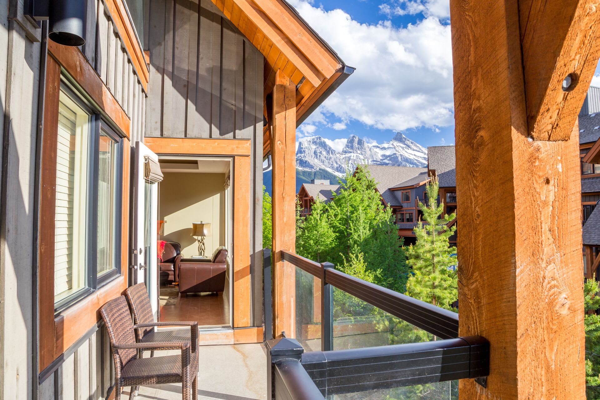 A balcony with a view of snow-capped mountains, wooden railings, and a seating area with a chair and a table.