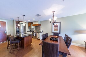 Una cocina moderna con una isla central, comedor con una mesa larga y sillas, y una araña.