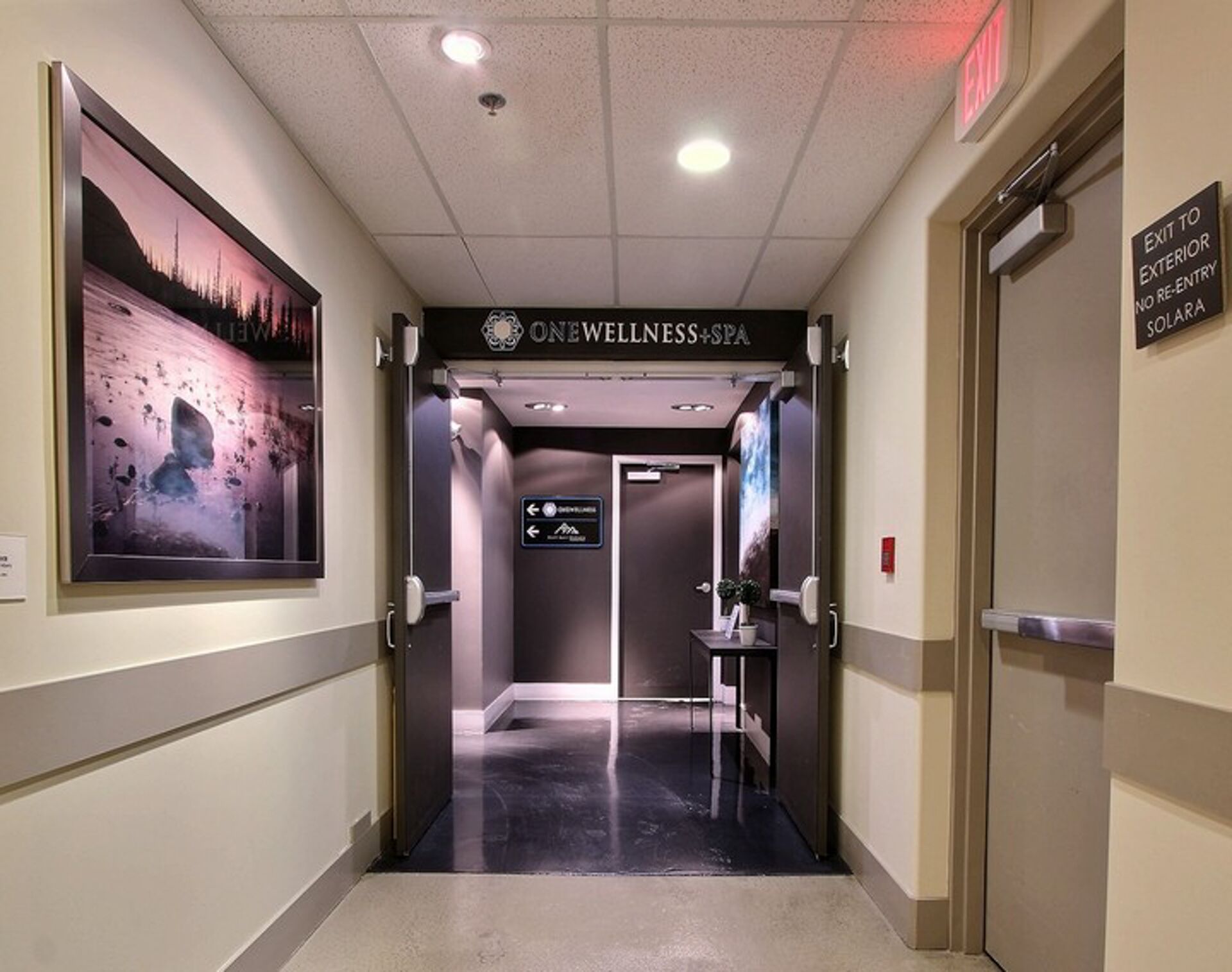 A hallway with a sign for 'ONEWELLNESS+SPA' leading to an elevator.
