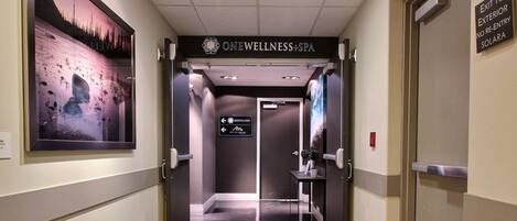 A hallway with a sign for 'ONEWELLNESS+SPA' leading to an elevator.