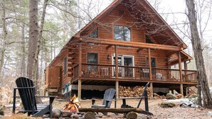 A log cabin with a balcony, a fire pit, and outdoor seating. - Secluded, Furnished, Log Home, Close To Many Adirondack Attractions. (Jay)