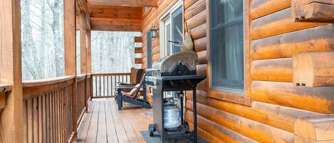 A wooden cabin with a porch, a grill, and a window.
