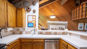 A kitchen with wooden cabinets, a stainless steel dishwasher, and a white countertop. - Deluxe CREEKSIDE Condo w/SPECTAULAR Mountain Views (Mammoth Lakes)