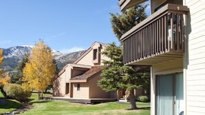 A modern building with a balcony, a well-maintained lawn, and a mountain backdrop. - Deluxe CREEKSIDE Condo w/SPECTAULAR Mountain Views (Mammoth Lakes)