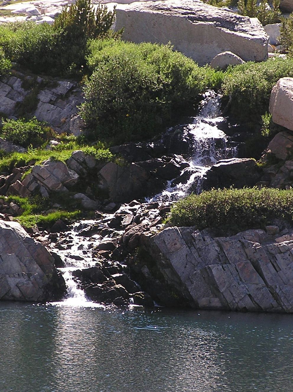 Un élément naturel composé d’une étendue d’eau et d’une cascade entourée de rochers et de végétation luxuriante.