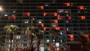 Un hotel de varios pisos con balcones, palmeras y una entrada con puerta de acceso.
