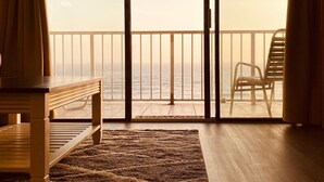 Una habitación con un banco de madera, un tapete y una silla orientada a un balcón con vistas al mar.