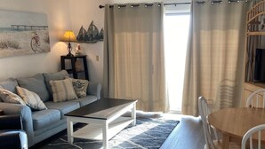 Una sala de estar con sofá, mesa de centro, alfombra, mesa de comedor, sillas y lámpara.