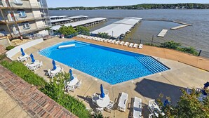 Une piscine avec des chaises longues et des parasols, une vue sur le bord de l’eau et un bâtiment doté de balcons.