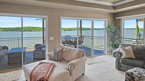Un vaste espace de vie doté d’une grande porte-fenêtre coulissante donnant sur un balcon avec vue sur un lac, et aménagé avec un canapé, un fauteuil et une table à manger.