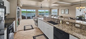 Cozinha com bancadas de granito, lava-louças e vista para um lago através de grandes portas de correr.