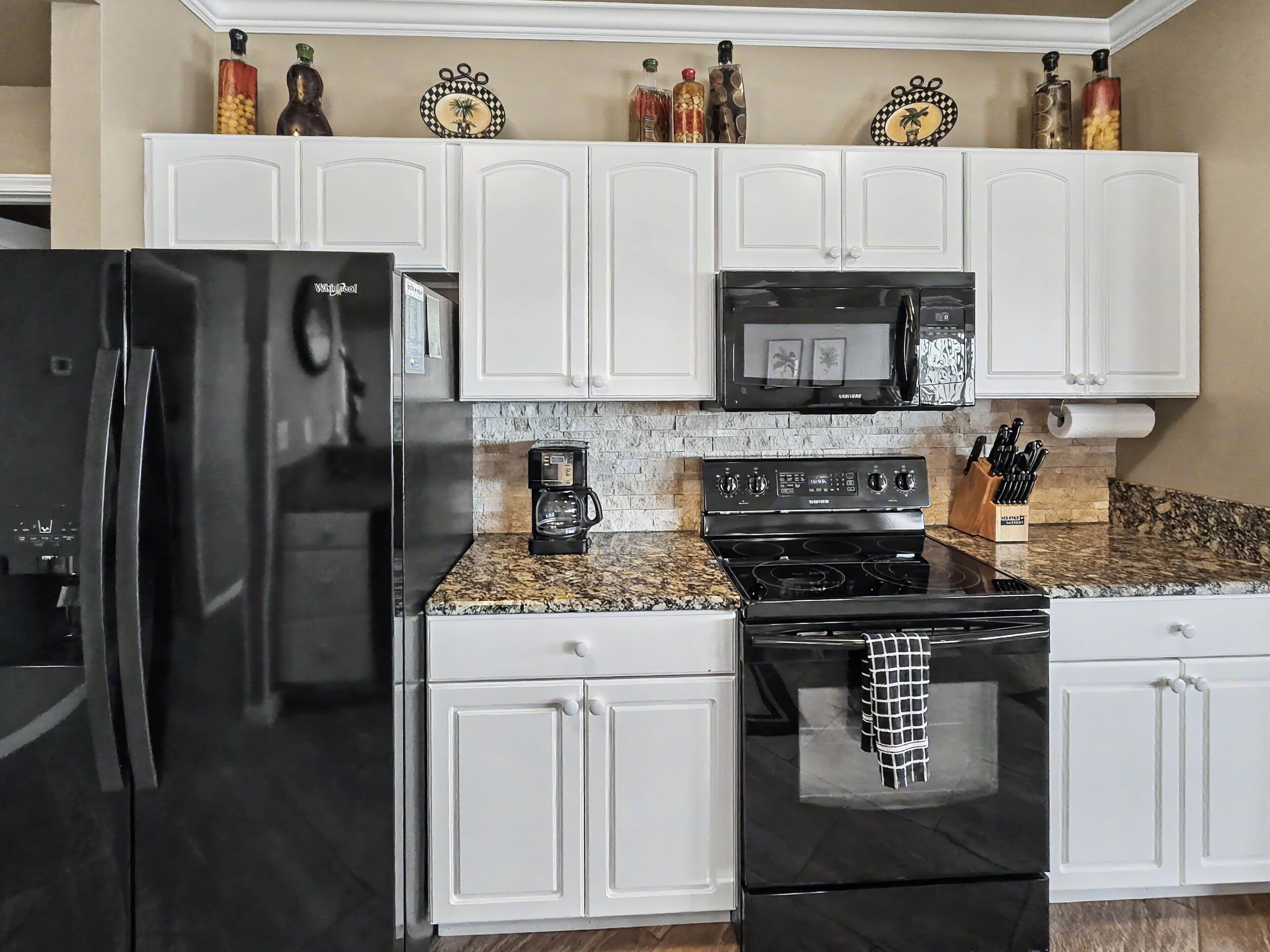 A kitchen with white cabinets, a black refrigerator, a microwave, a stove, and a coffee maker.