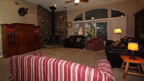 A cozy living room with a fireplace, a stone wall, a ceiling fan, and a large window. - Home in park like setting with 3 acre lake . (La Grange)