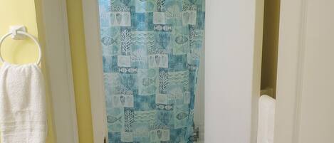 A bathroom with a shower curtain featuring a fish pattern, a white towel hanging on a ring, and a striped bath mat on the floor.
