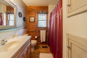 A bathroom with wooden walls, a white sink, a toilet, and a red shower curtain.
