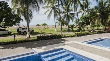 Uma piscina com água azul cristalina, rodeada por palmeiras e uma área gramada.