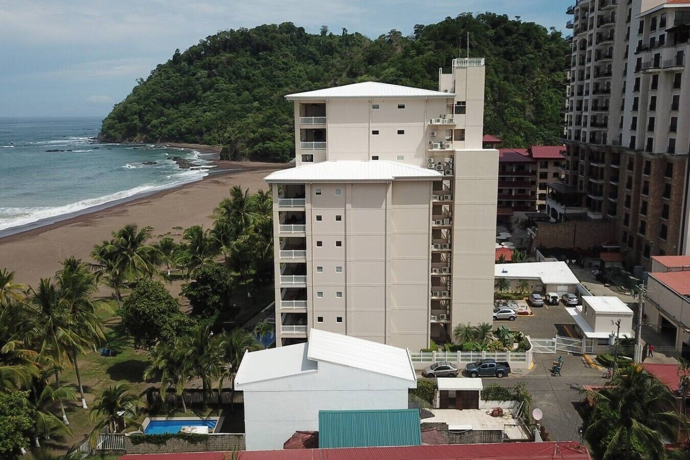 Un hotel de varios pisos con balcones, vista a la playa y zona de estacionamiento.