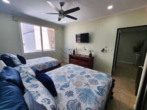 Habitación de hotel con dos camas, ventilador de techo, televisor de pantalla plana y un ventanal grande.