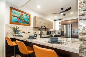 A modern kitchen with a marble countertop, stainless steel appliances, and a ceiling fan.